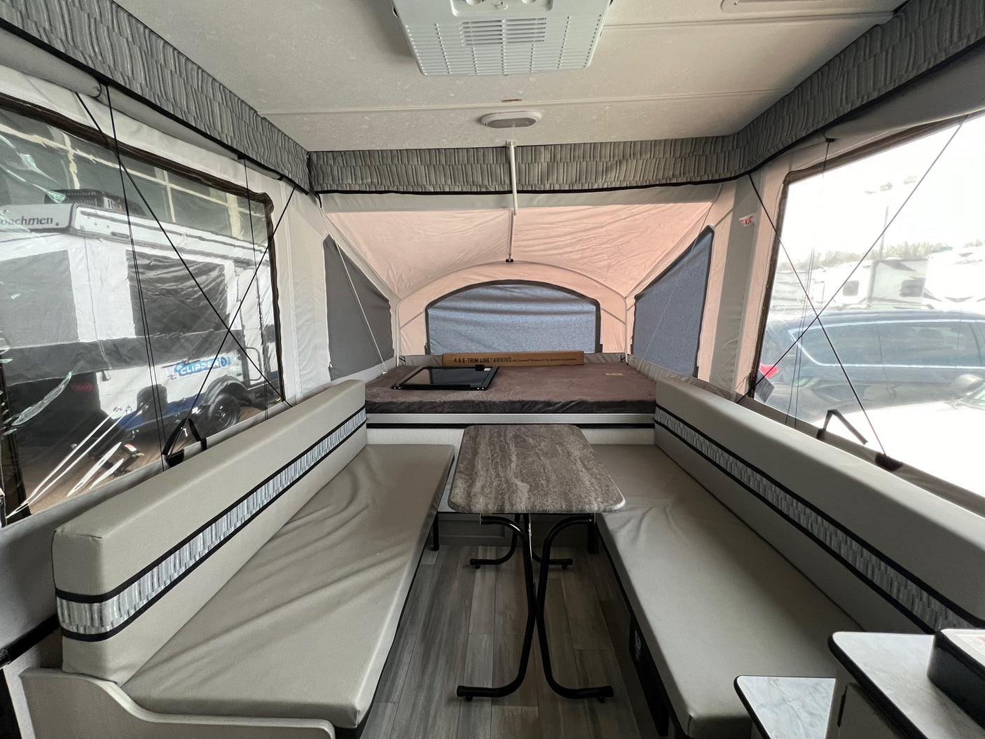 Interior of a light-toned pop-up camper RV rental, featuring a central dinette with benches and a rear bed.