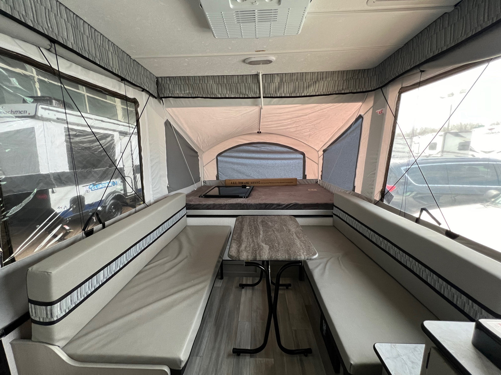 Interior of a light-toned pop-up camper RV rental, featuring a central dinette with benches and a rear bed.