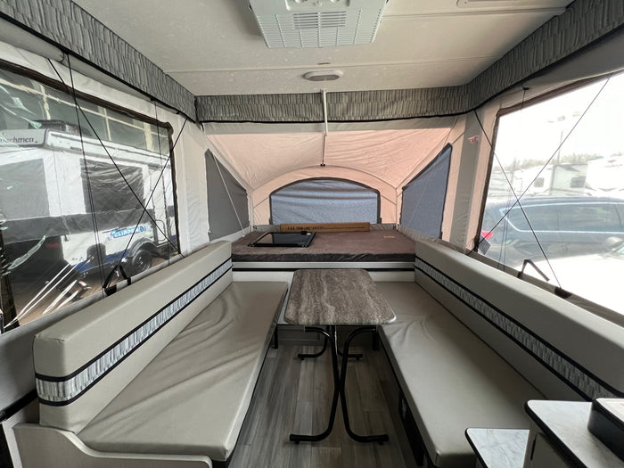 Interior of a light-toned pop-up camper RV rental, featuring a central dinette with benches and a rear bed.