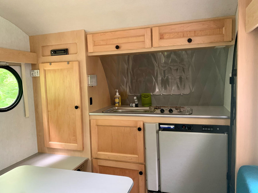 with chairs & cooler.|Inside a cozy RV rental: turquoise dinette cushions