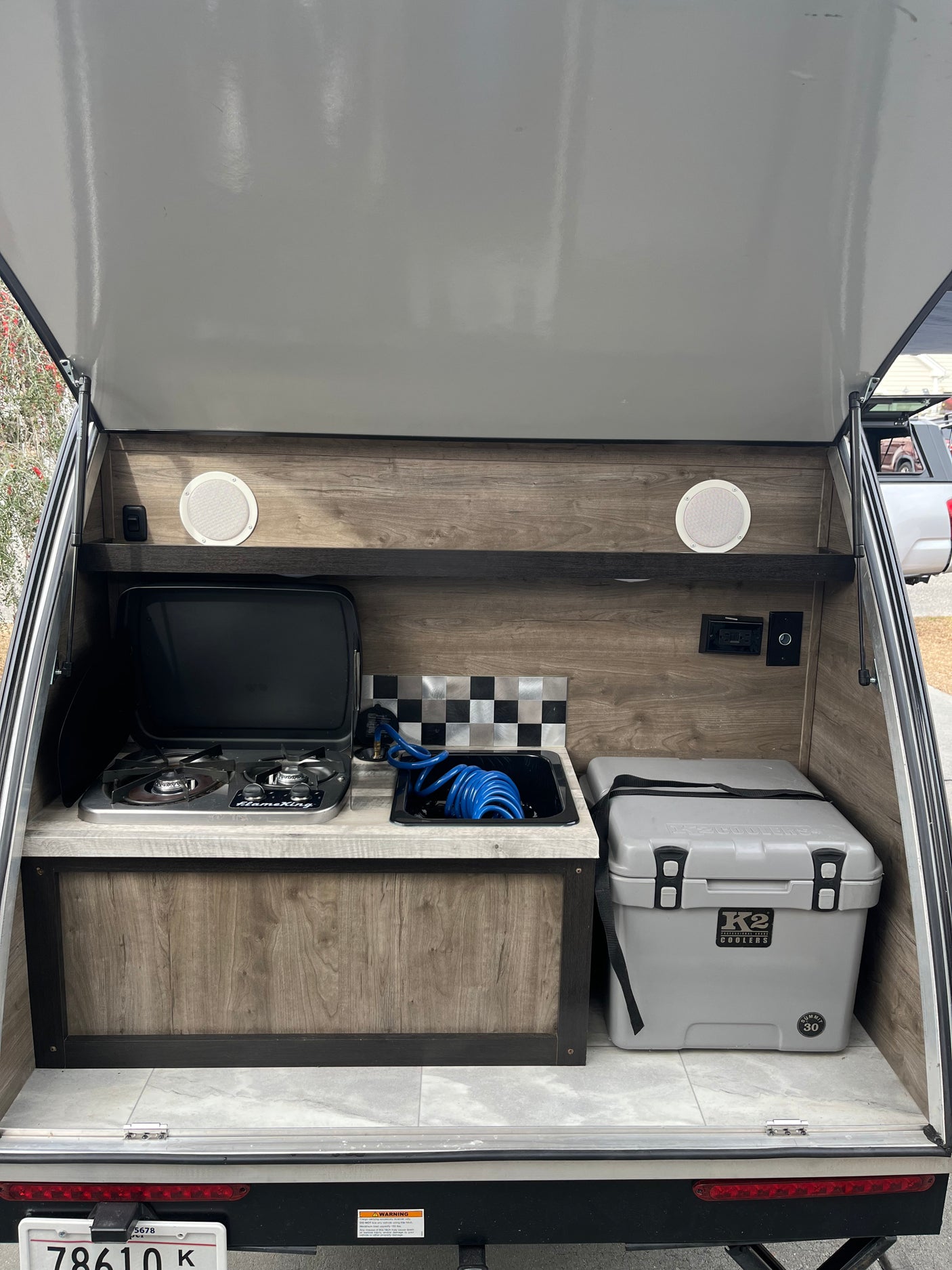 This rv rental features a compact outdoor kitchen with a FlameKing gas stove, sink, and large K2 cooler, ready for camping.