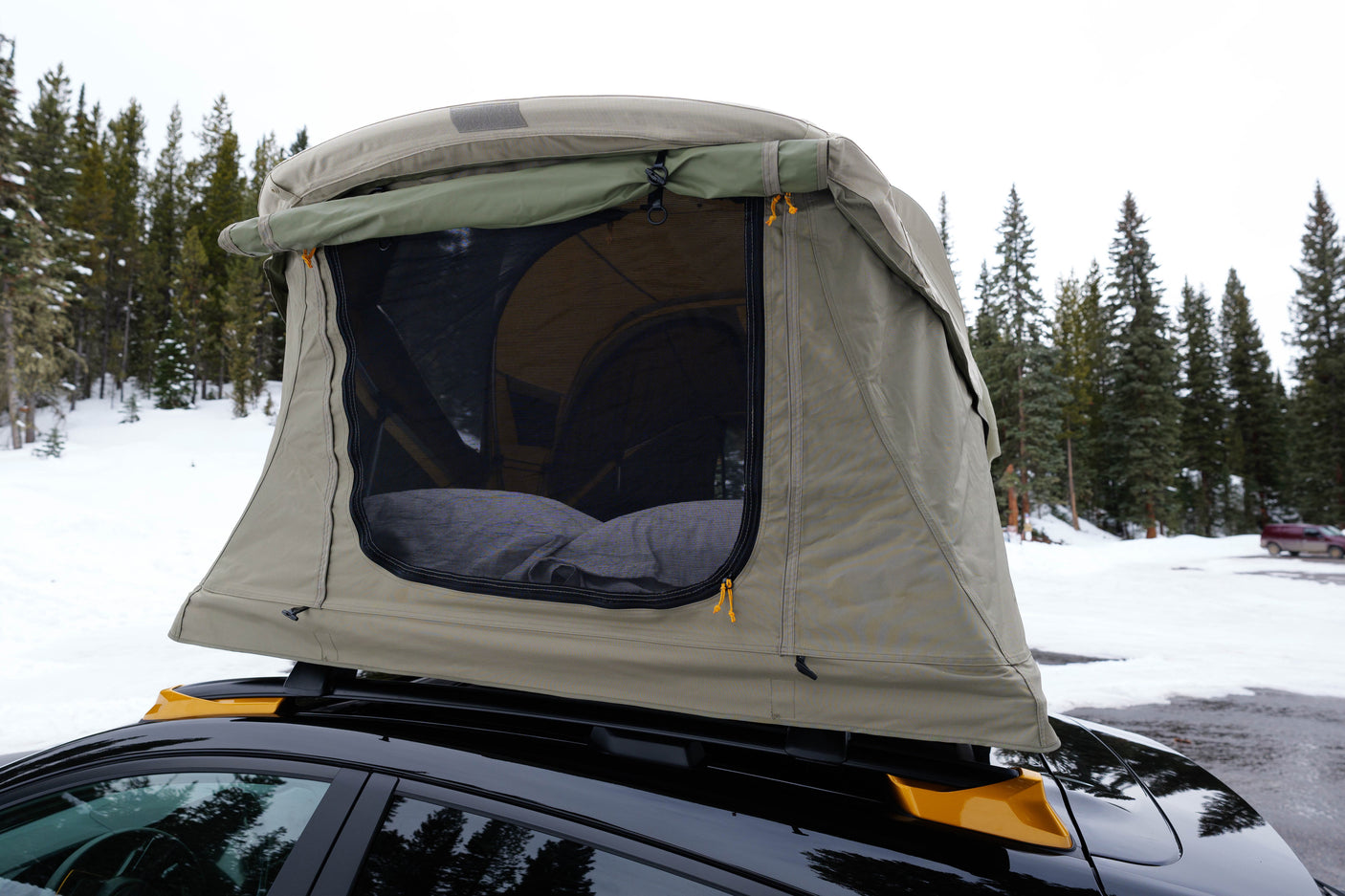 Car with a deployed rooftop tent, an **RV rental** alternative, for winter camping in the snowy forest.