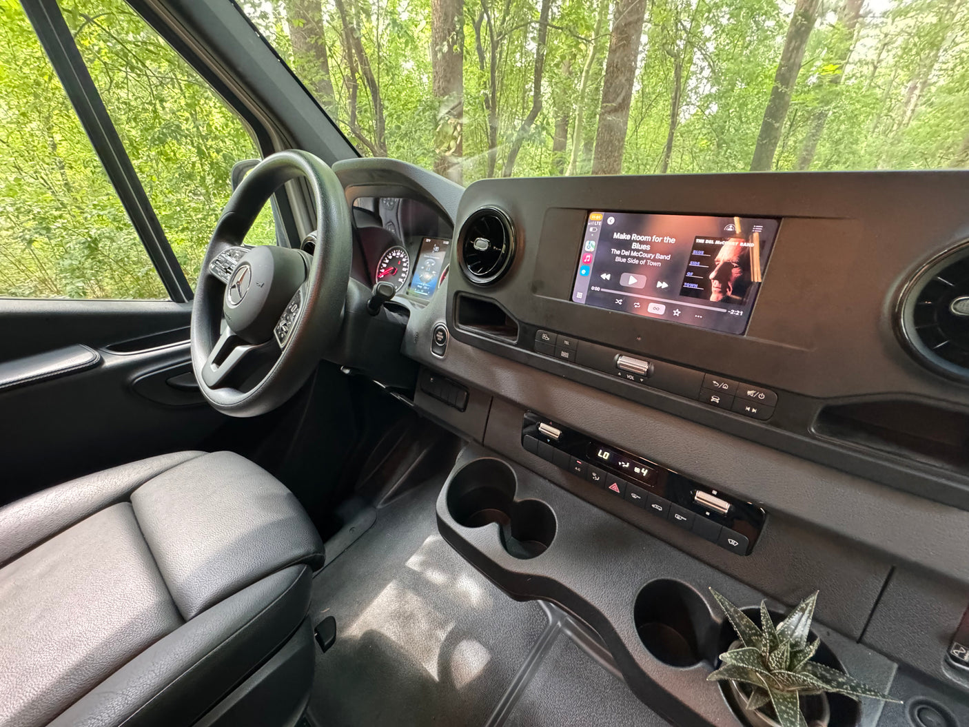 Experience comfort in this RV rental! Modern interior with dashboard, steering wheel, music playing, and a succulent plant by the cups.