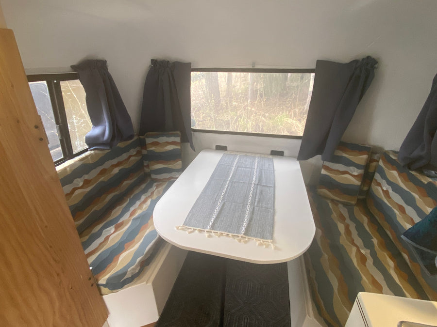 Cozy rv rental interior with a dining table, patterned cushions, and nature views from the windows.