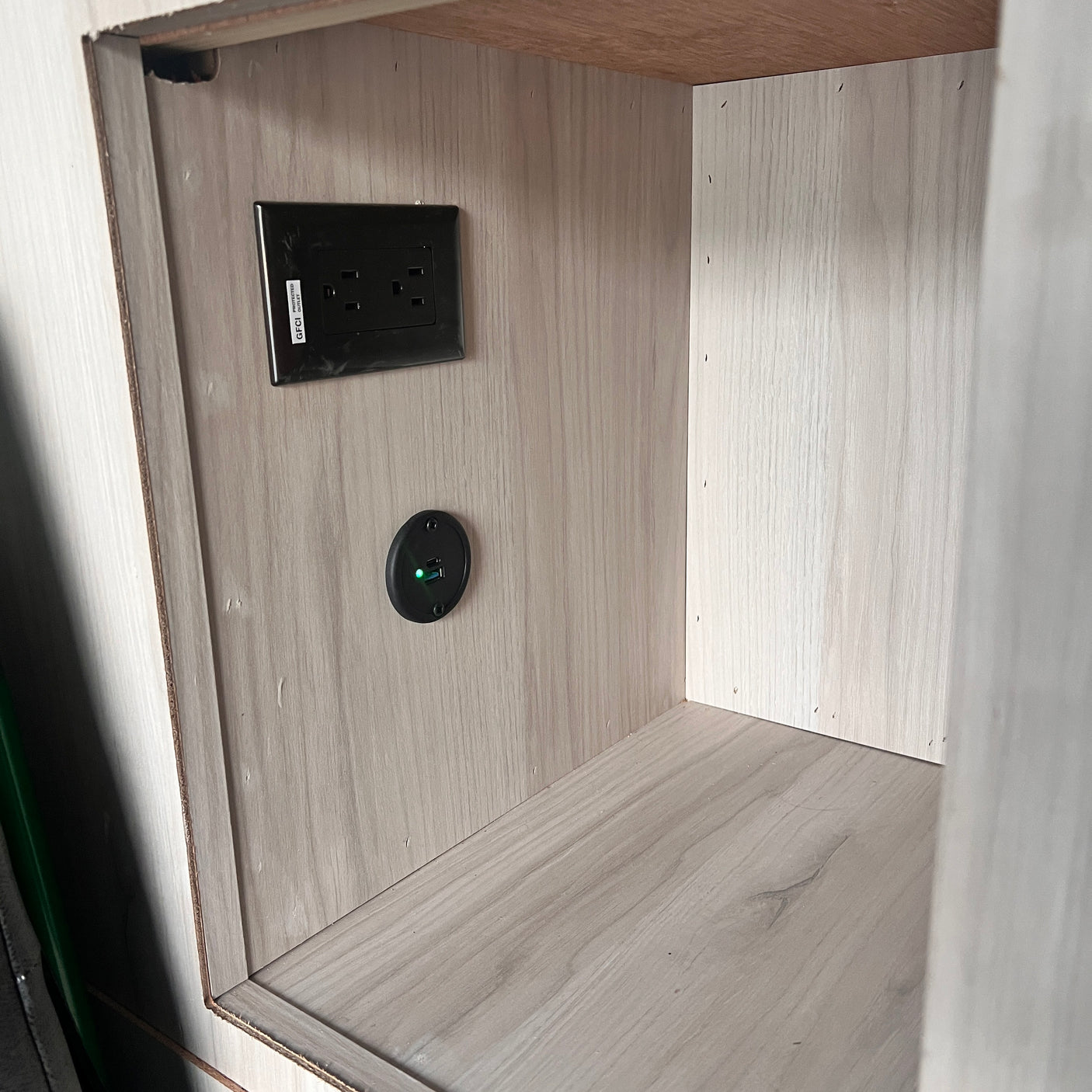 RV rental power access: a GFCI outlet and a glowing green USB charging port in a light wood cabinet.