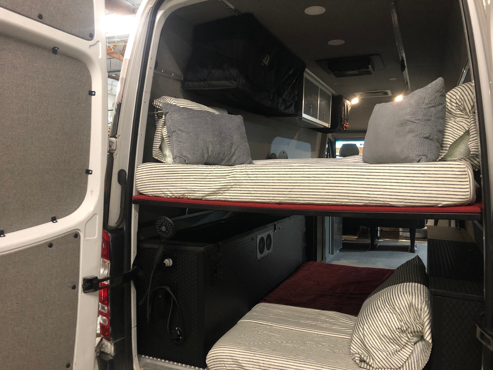 RV rental camper van interior with clever bunk beds, overhead storage, and a built-in shower, optimizing mobile living space.