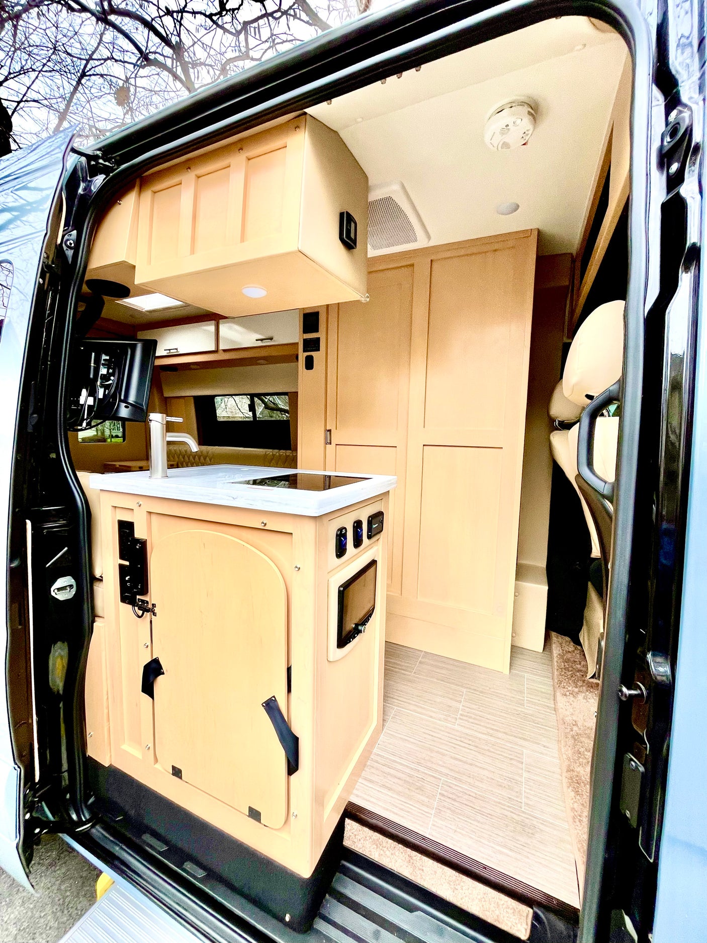 Detailed view of an rv rental's interior: modern kitchen with sink/stove, TV, light wood cabinets, and tiled floor.