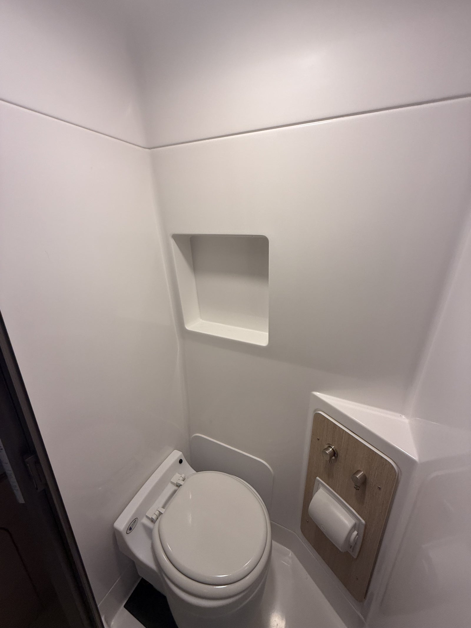 Compact, pristine all-white bathroom inside an RV rental, featuring a modern toilet and built-in shelf.