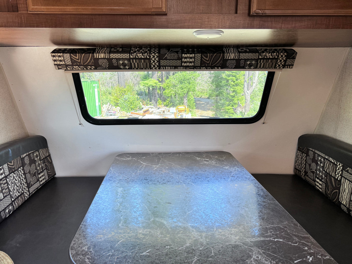 RV rental interior: A dinette area with a marbled table, patterned bench cushions, and a large window overlooking trees.
