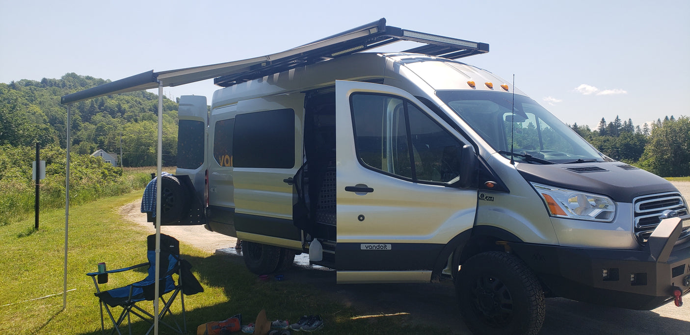 Rugged silver Ford Transit 4x4 camper van with awning & gear set up, ideal for your RV rental adventure.