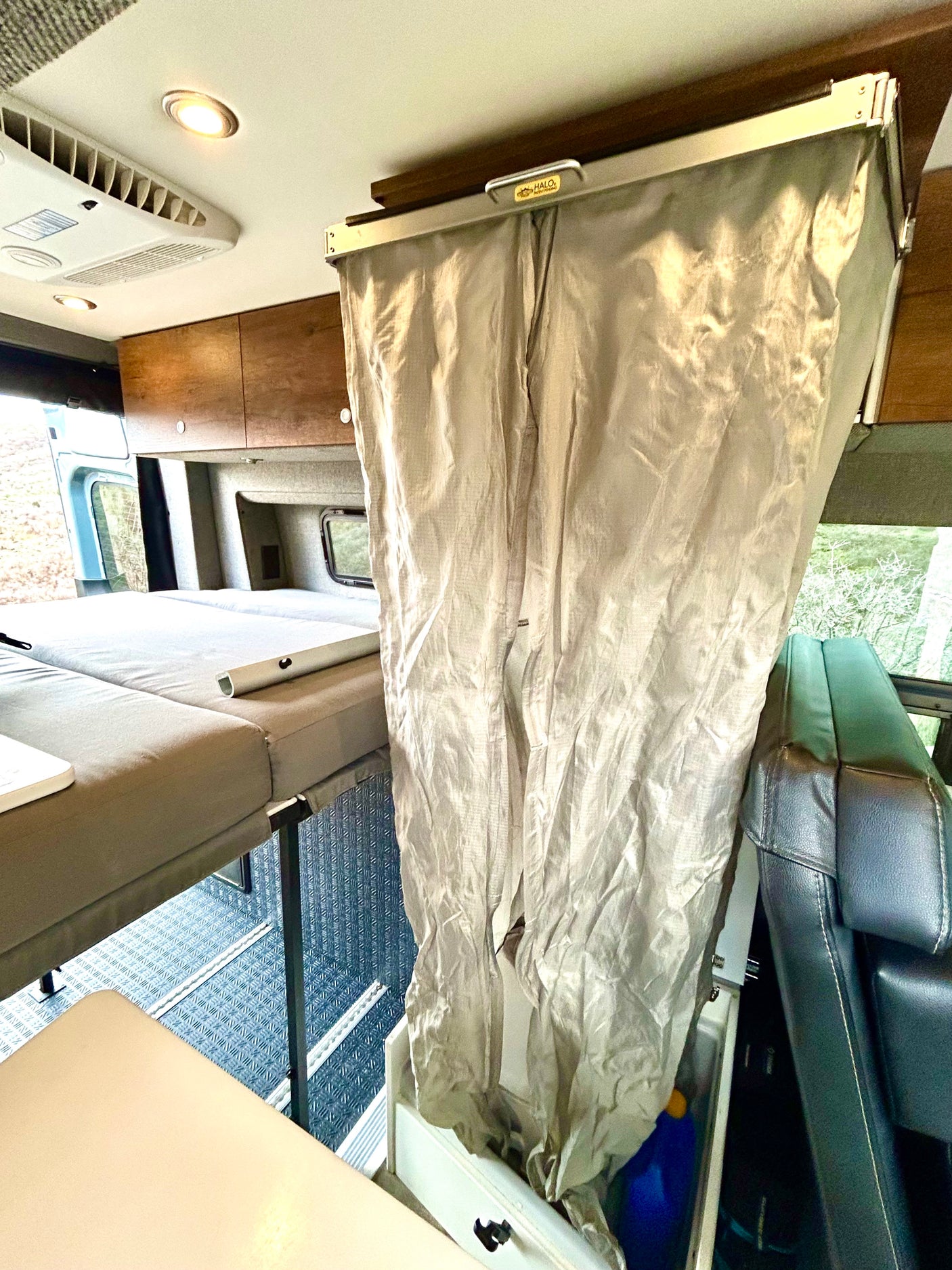 Inside an RV rental, showing a raised bed, a beige privacy curtain, and a black leather seat in the living area.