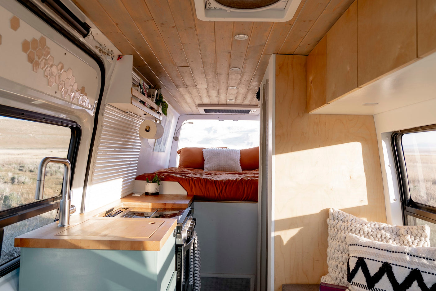 Spacious and bright RV rental interior featuring a modern kitchen with a sink & stove, and a cozy bed, perfect for van life adventures.
