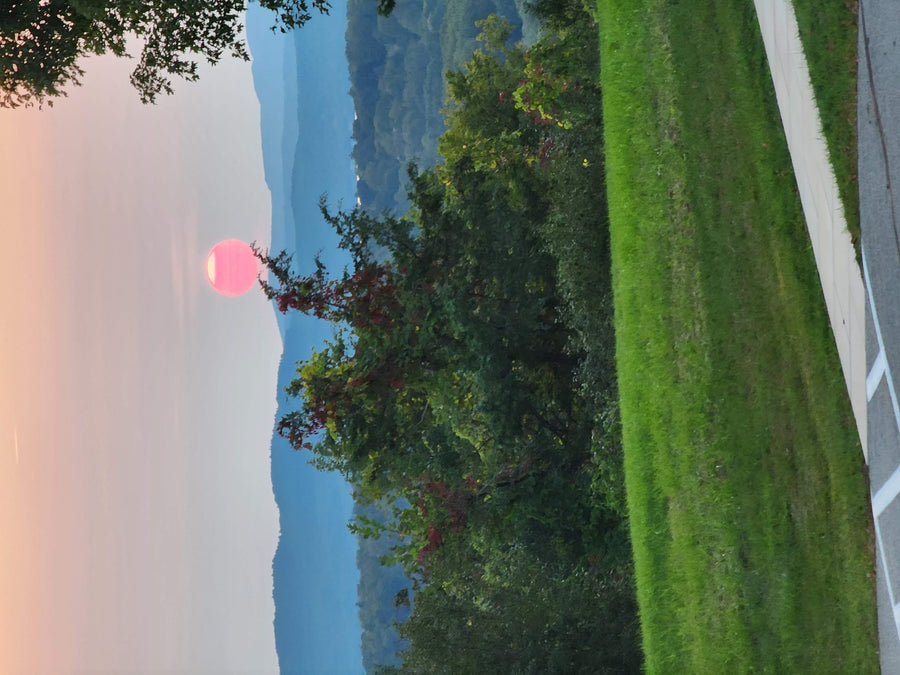 & fire pit under an overcast sky.|Striking pink sun sets over serene blue mountains and vibrant green trees