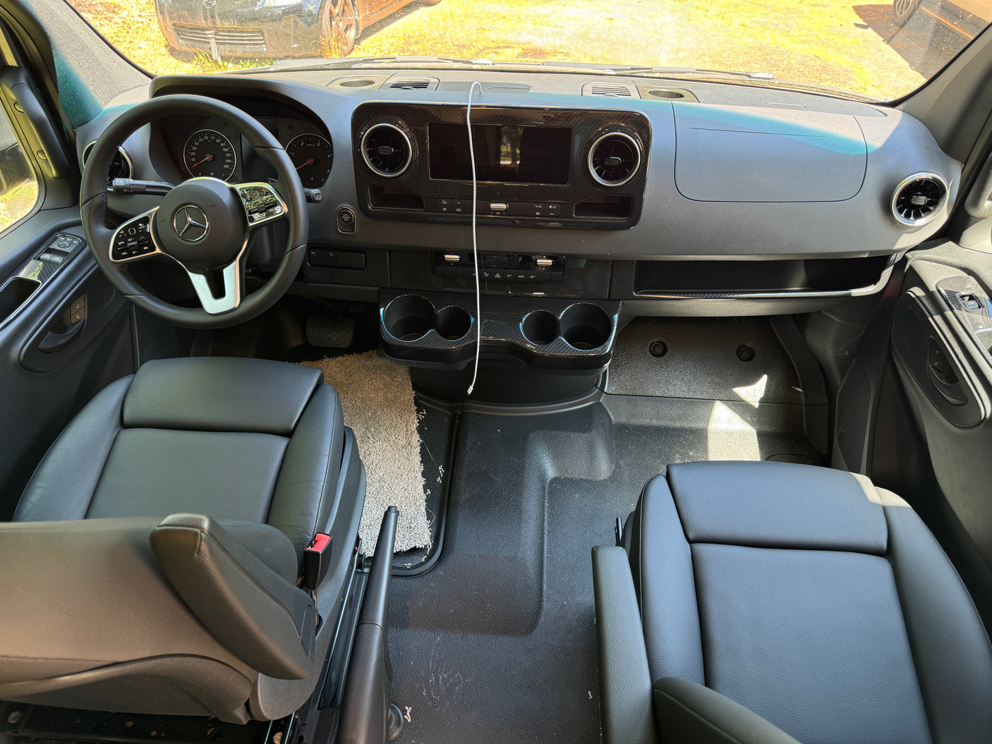 Front cabin of an RV rental, showcasing a modern Mercedes dashboard, steering wheel, and comfortable black leather seats.