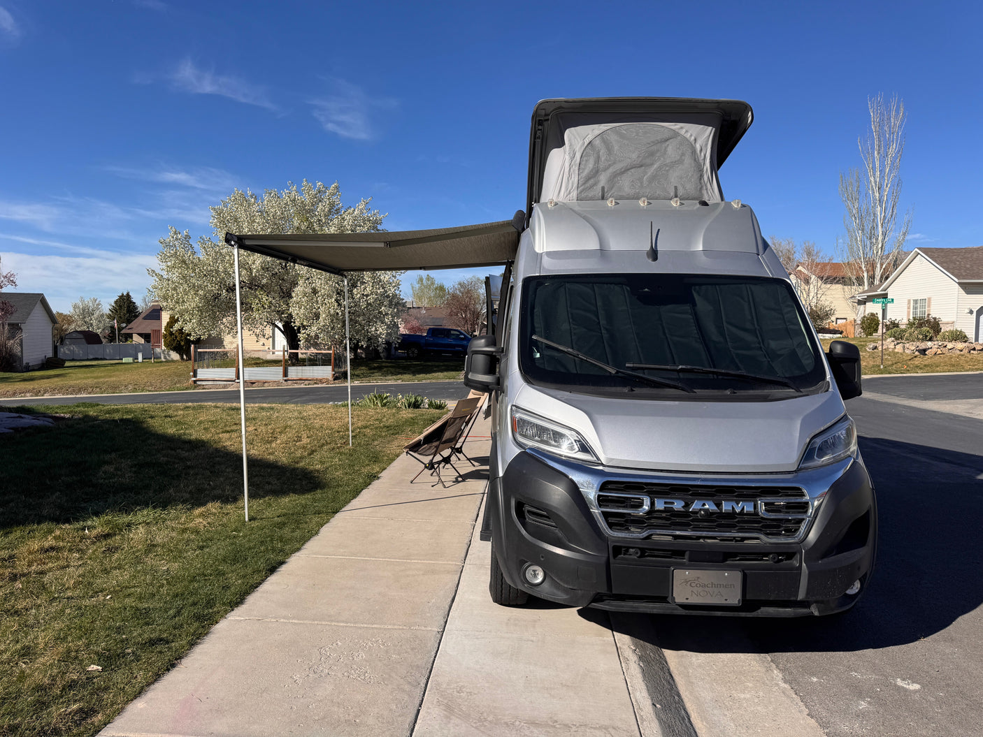 Silver Coachmen Nova camper van with pop-top & extended awning, parked on a sunny street. An ideal RV rental for your next adventure!
