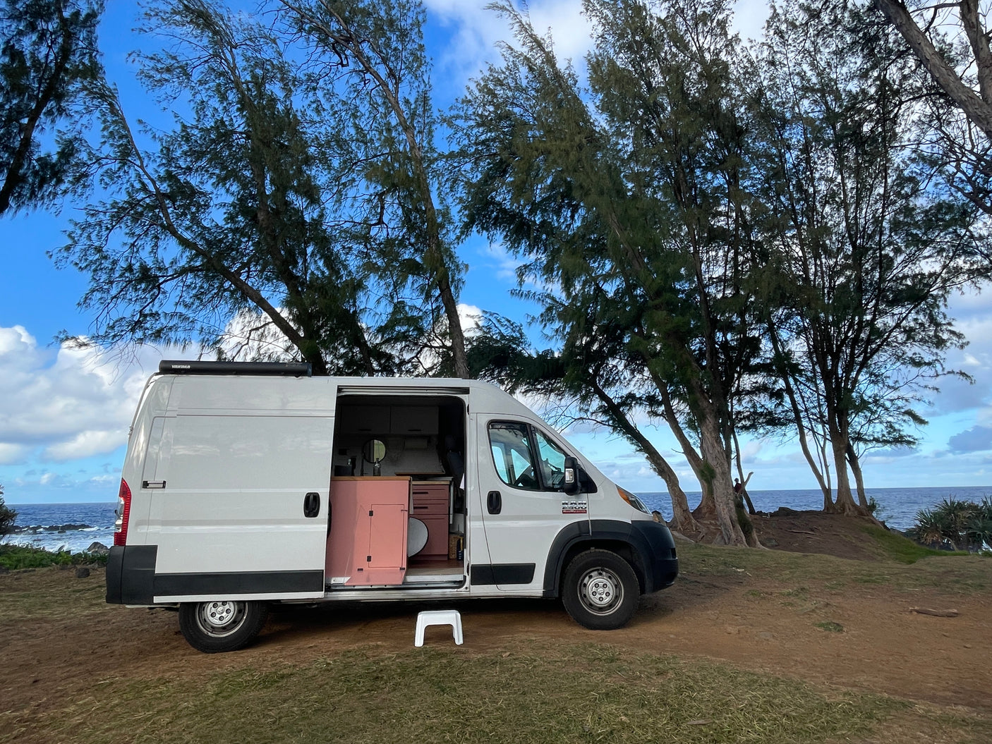 This white RV rental camper van with a stylish pink interior is perfectly parked overlooking a beautiful ocean.
