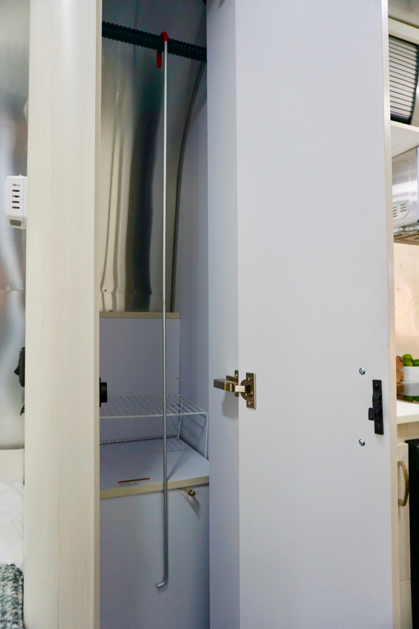 RV rental interior: open wardrobe reveals wire shelf, long pole, and metallic walls. Practical compact storage for travelers. — photo 18