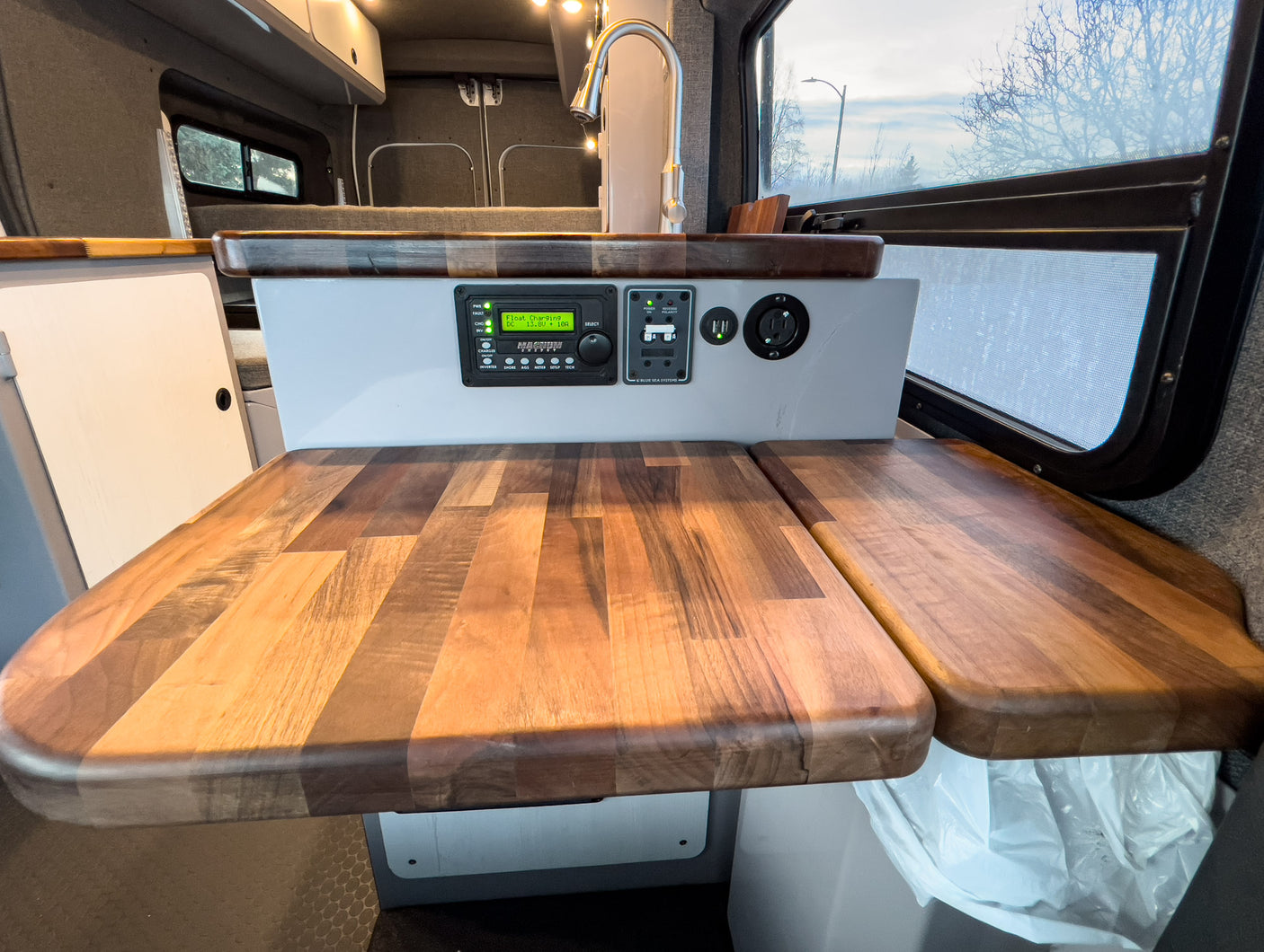 Modern RV rental kitchen with wood counters, smart control panel, and faucet.