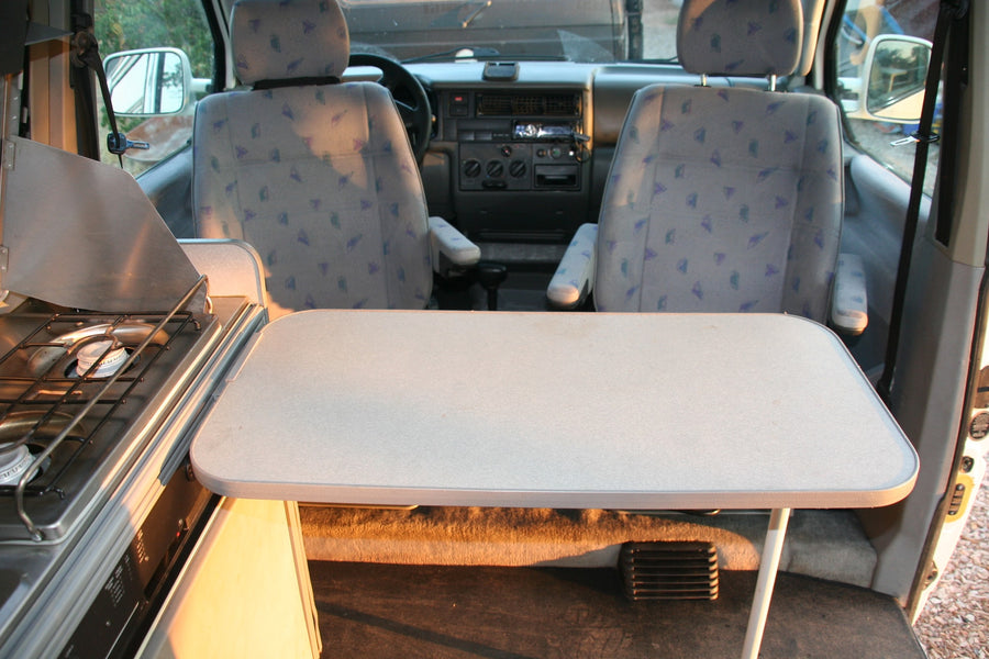 Inside an RV rental: kitchen with stove, dining table set up, and front seats visible, ready for travel adventures.