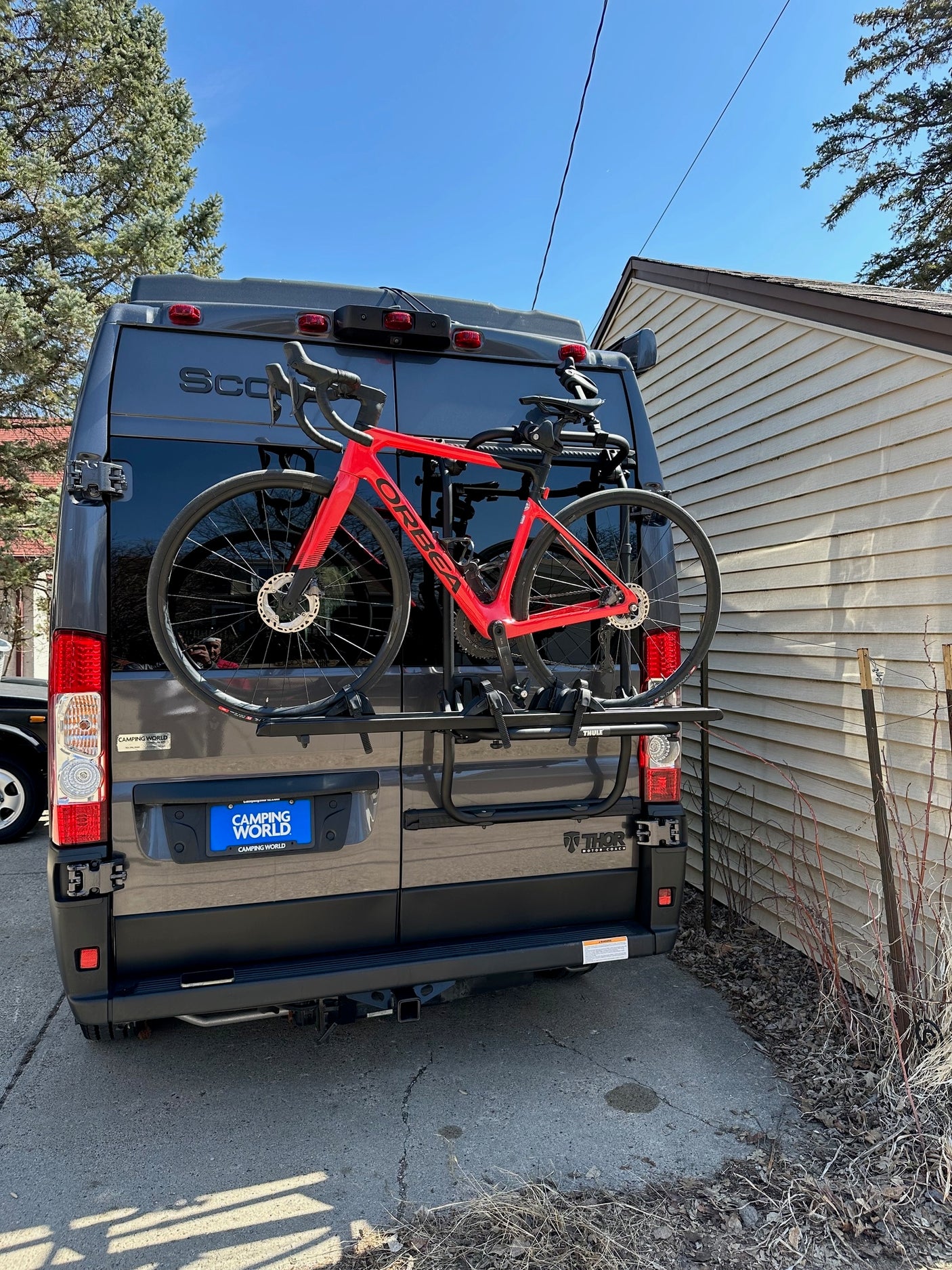 A dark gray Thor RV rental with a Camping World license plate, carrying a red Orbea road bike on its rear rack.