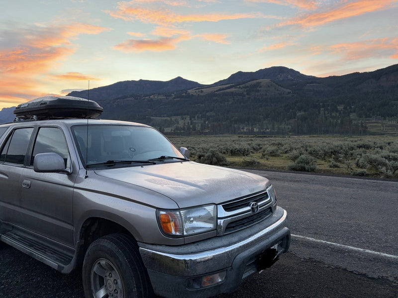 Front three-quarter view of the 4Runner with rooftop cargo box, mountains and sunrise sky in the background — photo 4