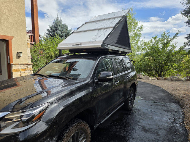 Terrapod RTTx XL hardshell rooftop tent fully deployed on a black Lexus GX460, shot from the driver's side, showing the white topo-print hard shell propped open in a wedge over the grey tent body