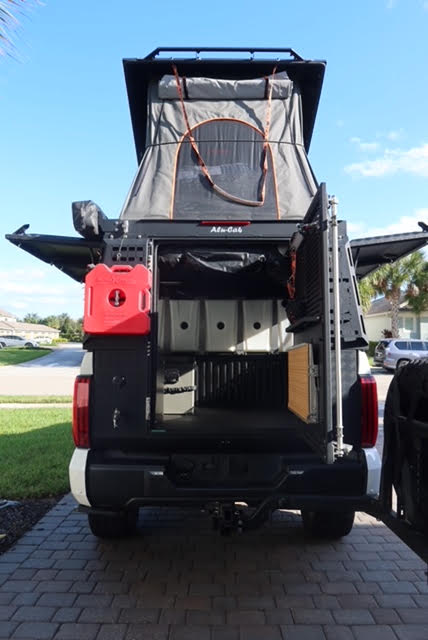 Straight rear view with the tailgate down and both gull-wing doors open, camper roof raised with the bug-netted tent walls visible, Rotopax fuel cell and the interior fresh water tanks in the bed — photo 6