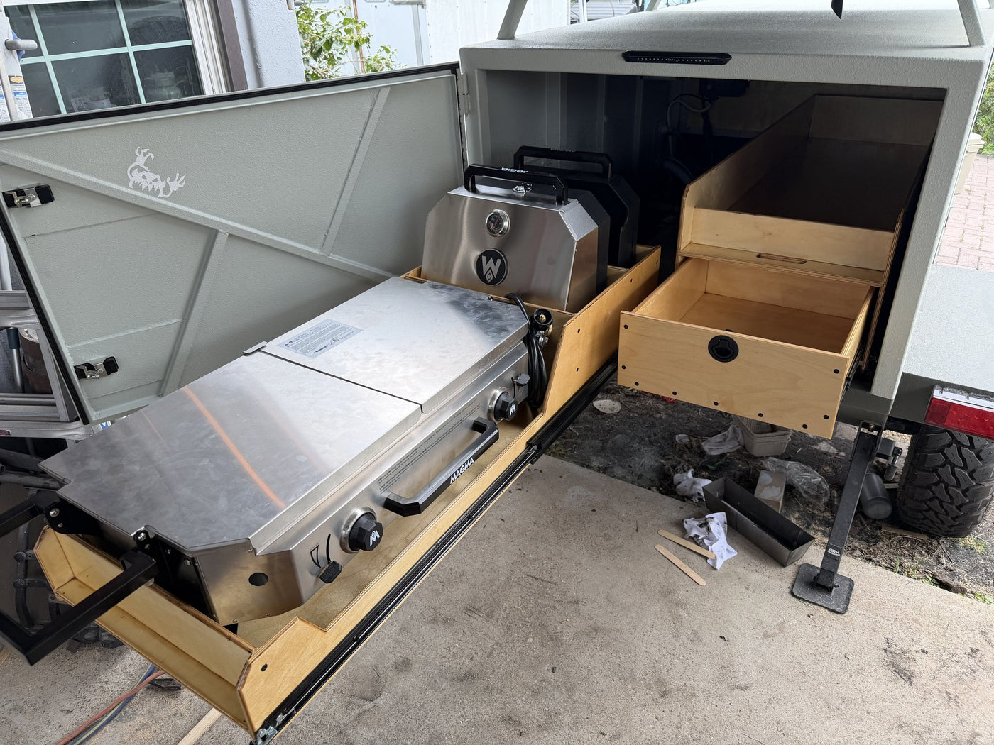 Both rear drawers pulled fully out in daylight, showing the mounted Magma Crossover double burner with grill and griddle tops on the driver side and the empty birch storage drawer on the passenger side — photo 4
