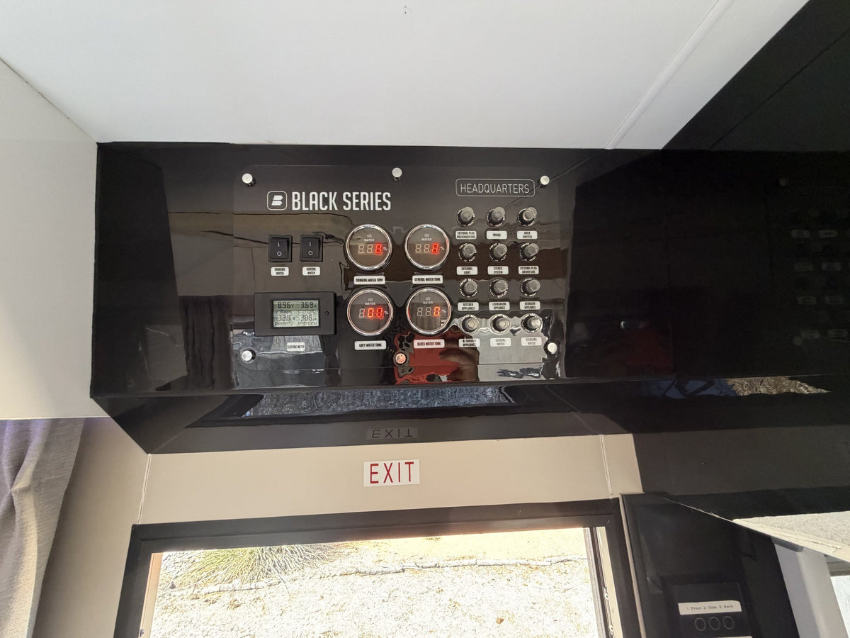 Black Series HEADQUARTERS control panel above the entry door with digital gauges for the drinking, general, grey and black water tanks, battery voltage display and labelled switches for lighting, fridge, pumps and appliances — photo 9