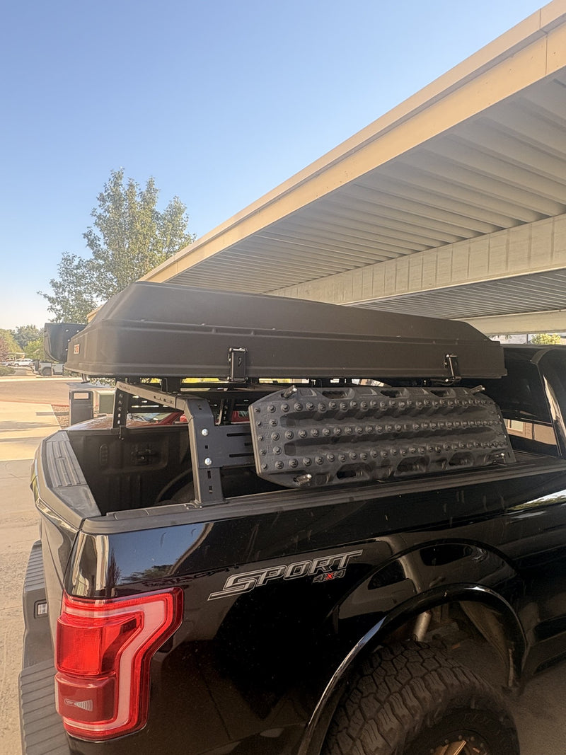 Rear three-quarter view of the closed hardshell tent on the bed rack, with two textured traction boards mounted to the rack's side panel above the truck bed — photo 2