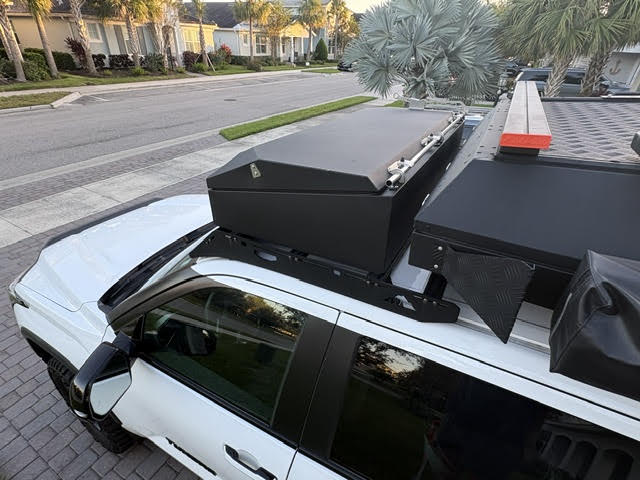 The sealed Alu-Cab wood storage box mounted on the cab roof rack above the Tundra's sunroof, alongside the camper's checker-plate side and rolled awning — photo 14