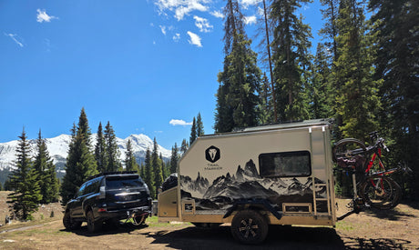 Trail Marker off-road trailer parked in an alpine forest below snowcapped peaks