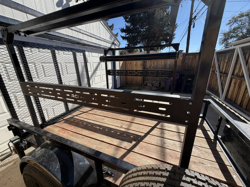 Deck-level view of the slotted RCI accessory crossbar mounted across the rack with the black roller bar above it, showing the deck tie-down track and the mesh gate standing at the rear — photo 8