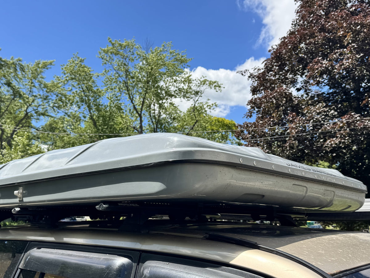 Side profile of the closed James Baroud hardshell tent mounted on a roof rack, showing the shell depth and mounting rails — photo 3