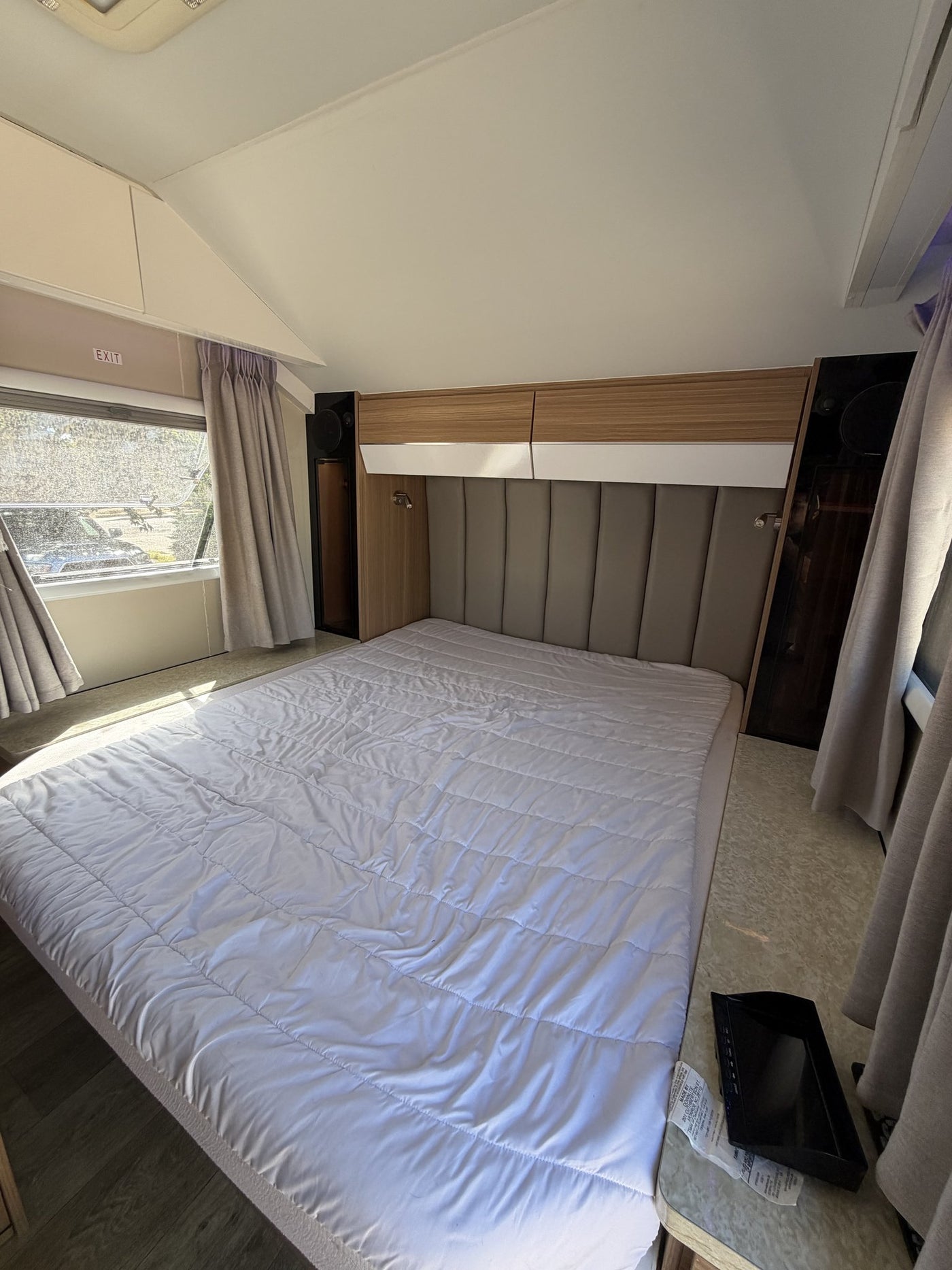 Rear bedroom with the queen bed made up, upholstered padded headboard, overhead storage lockers with reading lights, wardrobe, and curtained windows on both sides — photo 8