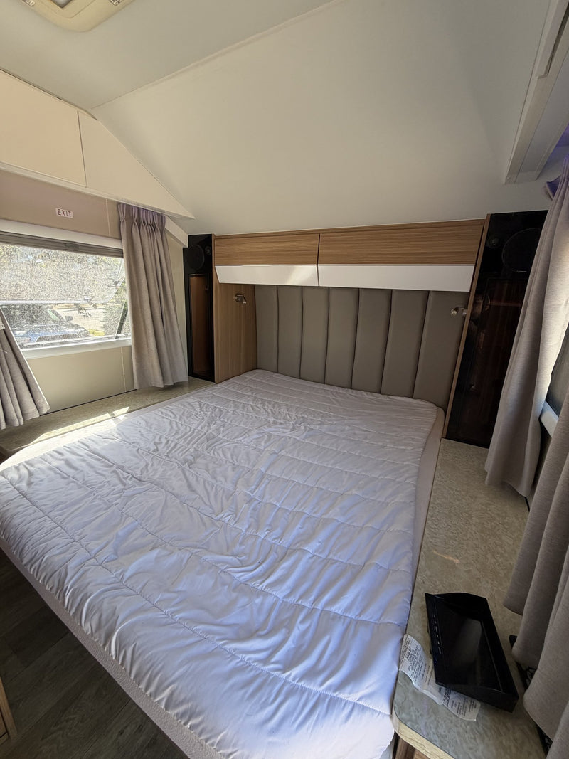 Rear bedroom with the queen bed made up, upholstered padded headboard, overhead storage lockers with reading lights, wardrobe, and curtained windows on both sides — photo 8
