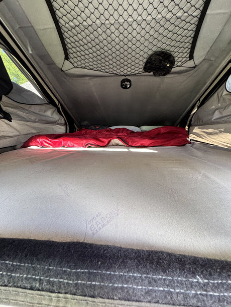 Interior of the tent showing the mattress, overhead storage net and ceiling-mounted exhaust fan