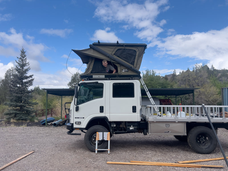 Isuzu NPR expedition rig at camp with rooftop tent open — photo 3