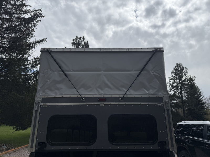 Straight-on rear view of the camper with the pop-top raised and the rear hatch closed, showing the two large tinted rear windows, centre brake light and the tensioned canvas of the pop-top — photo 3