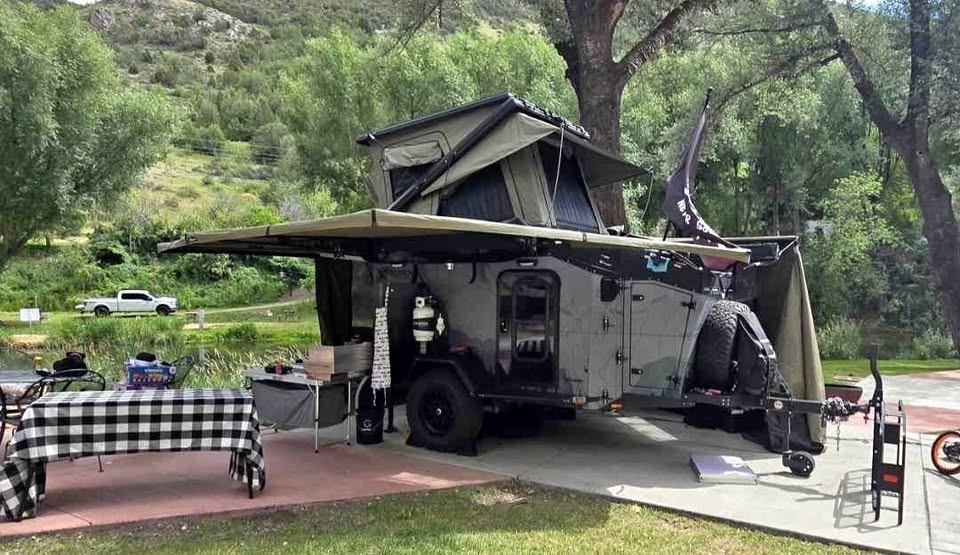 XPedition Voyager Sky XE set up at a creekside campsite with the 270 awning extended, camp kitchen table and chairs out, rooftop tent open under the trees — photo 15