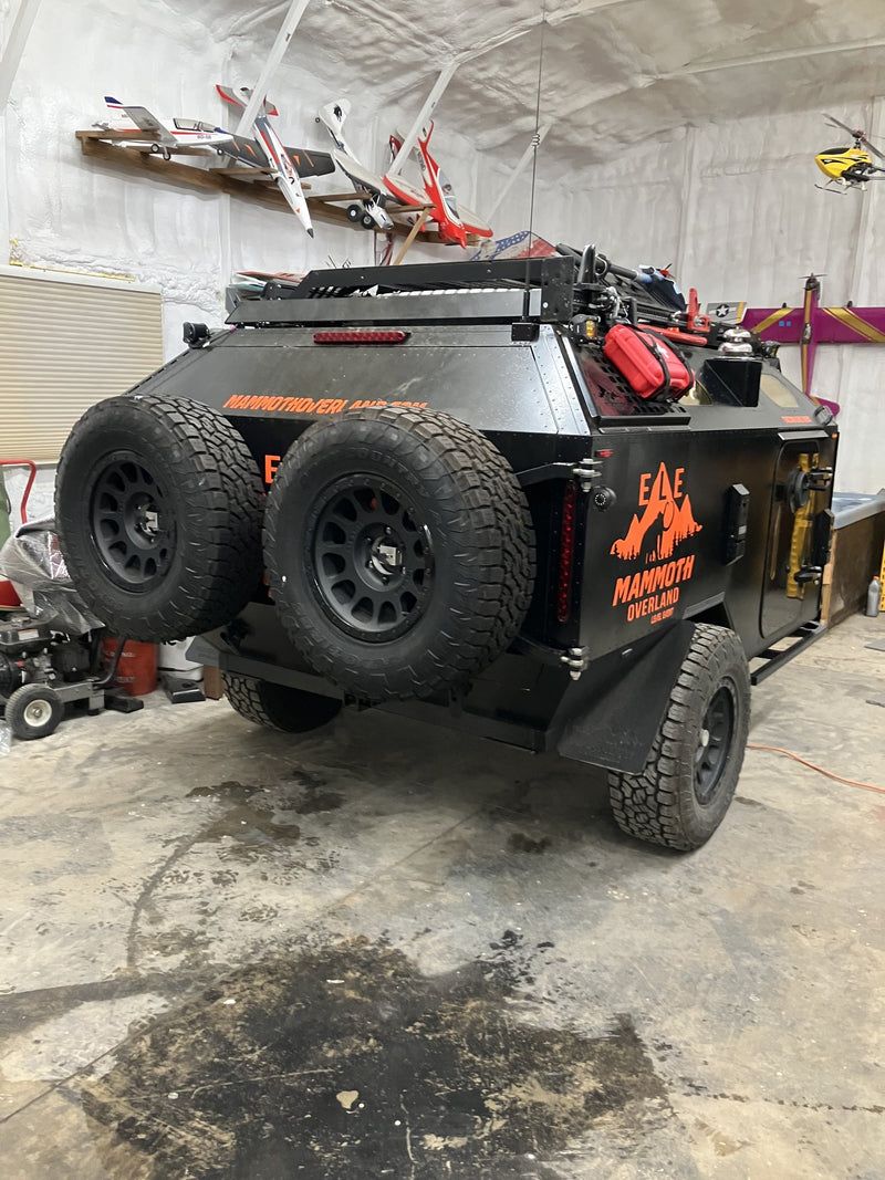Rear three-quarter view of the 2023 Mammoth Overland ELE off-road trailer showing two full-size spare tires on the rear carrier, the LED tail light bar, the ELE and MAMMOTH OVERLAND graphics, and the roof rack with a fuel can — photo 3