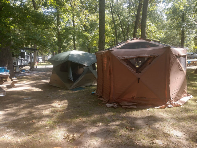 Gazelle G6 Cool Top six-sided portable gazebo in Badlands Brown, set up on a wooded campsite with the screen walls zipped closed and the shade roof deployed