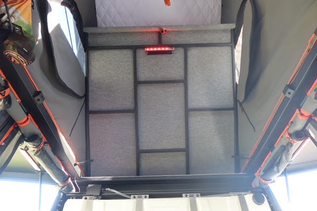 Looking up into the raised camper roof showing the grey mattress and topper on the roof platform, dual-colour LED touch light and the orange-strapped tent walls on both sides — photo 9
