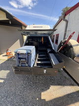 Rear view of the Extendobed system slid out of the truck bed under a canopy and rooftop tent, showing the divided drawer compartments and the strapped ARB fridge
