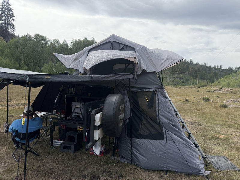 The tent and annex in use at camp, rear quarter view showing the annex fully zipped, guy lines staked out and the ladder secured along the outside — photo 4