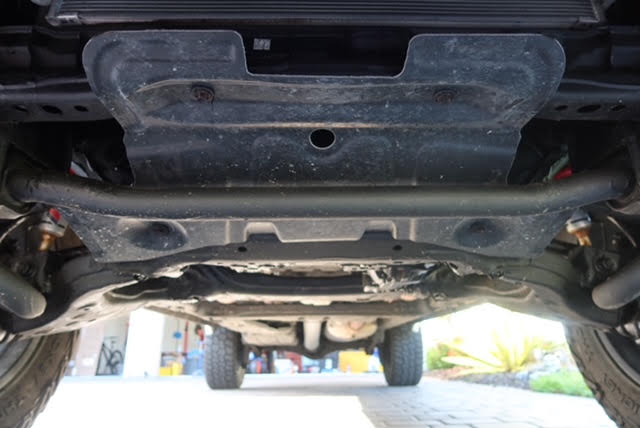 Underbody view showing the factory skid plate and the NH Oil permanent protective undercoating applied across the frame and crossmember — photo 17