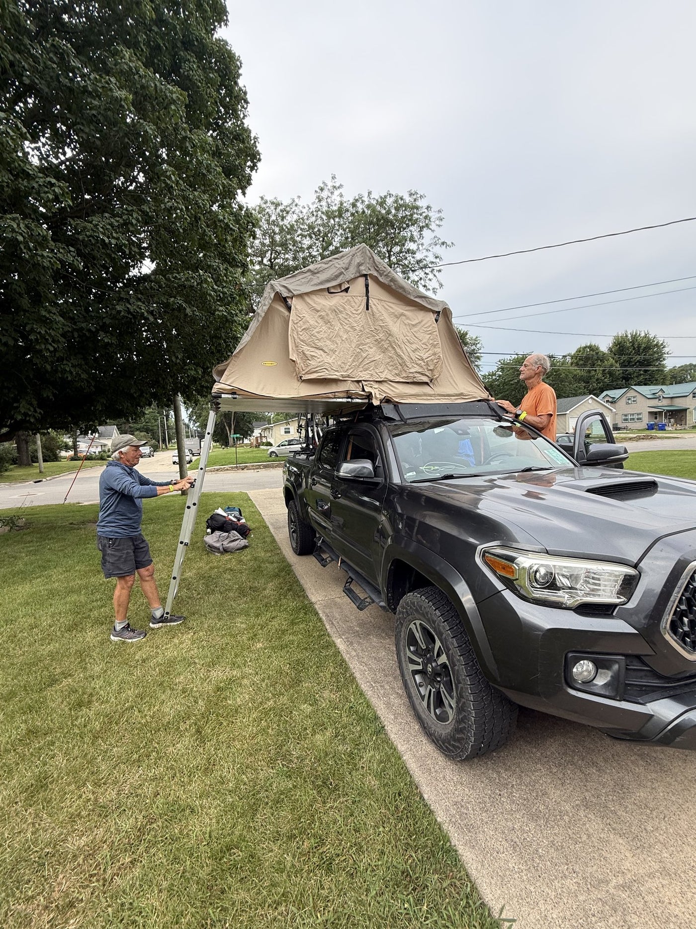 Two people setting the tent up on a grey pickup, showing how it folds out over the side of the truck — photo 13