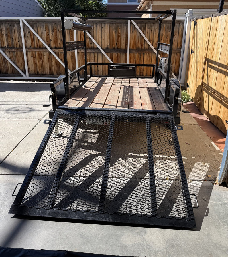 Rear view with the expanded metal mesh gate dropped flat as a loading ramp, looking up the wood-plank deck toward the front rack panel and the mounted spare tire — photo 5