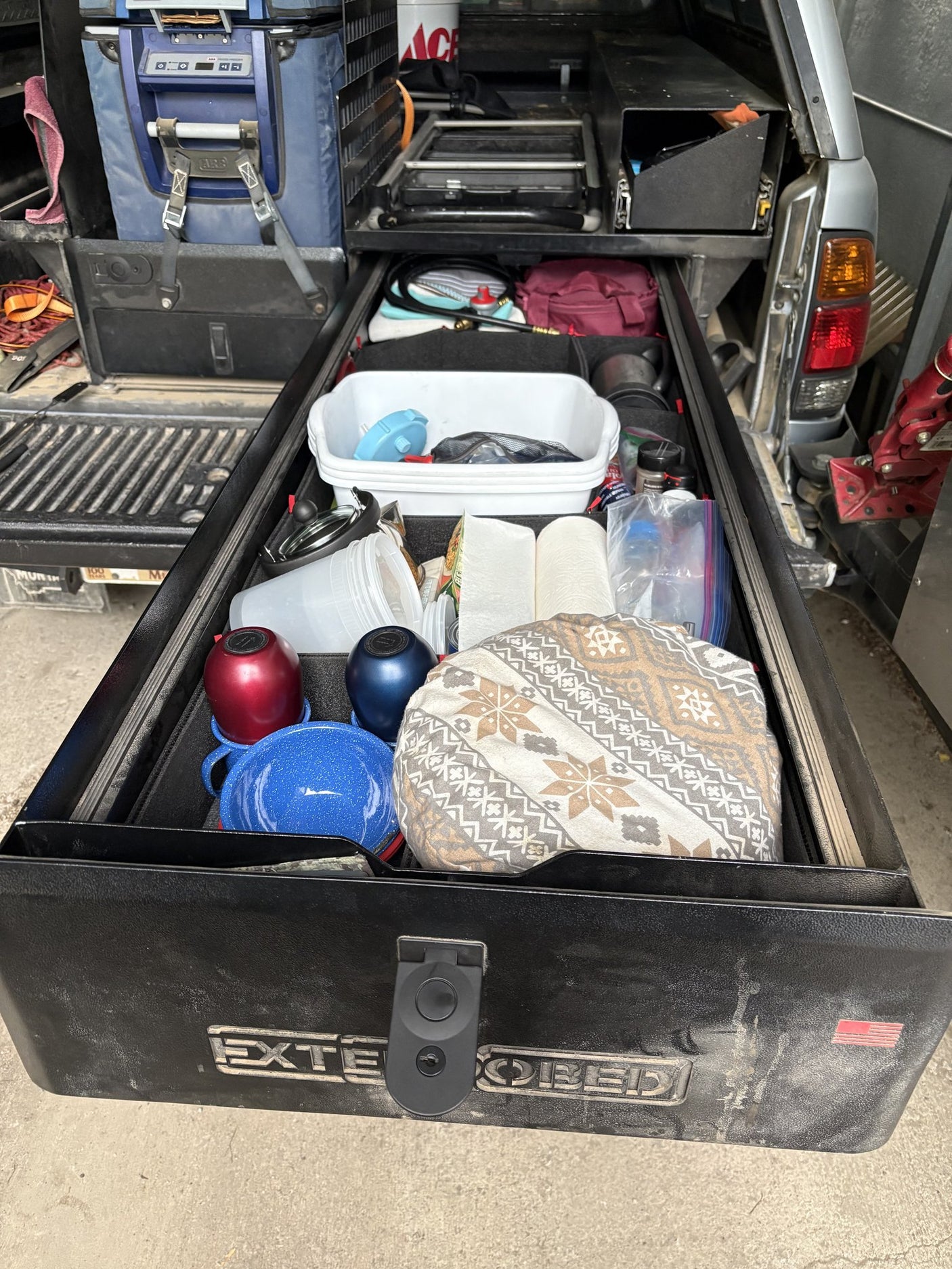 Deep kitchen drawer open, packed with cookware, enamel pots, water bottles and food storage containers in the foam organizer
