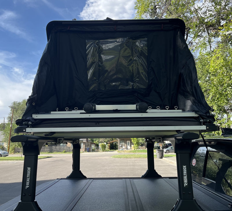 Rear view of the tent open, showing the blackout door panel, clear window and the aluminum floor rails mounted to the RealTruck bed rack legs — photo 3